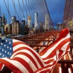 American flag in front of the Brooklyn Bridge and the New York City skyline, illustrating US infrastructure pressures and power grid challenges in 2026.