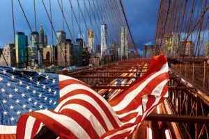 American flag in front of the Brooklyn Bridge and the New York City skyline, illustrating US infrastructure pressures and power grid challenges in 2026.